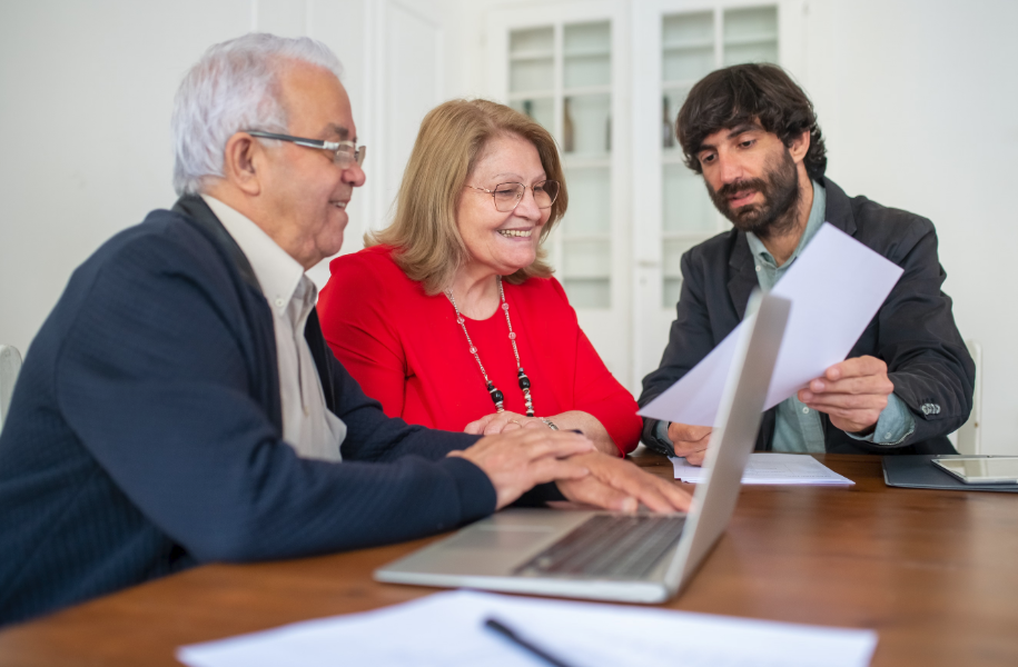 Three people in a meeting at a table, discussing documents with a laptop in the foreground