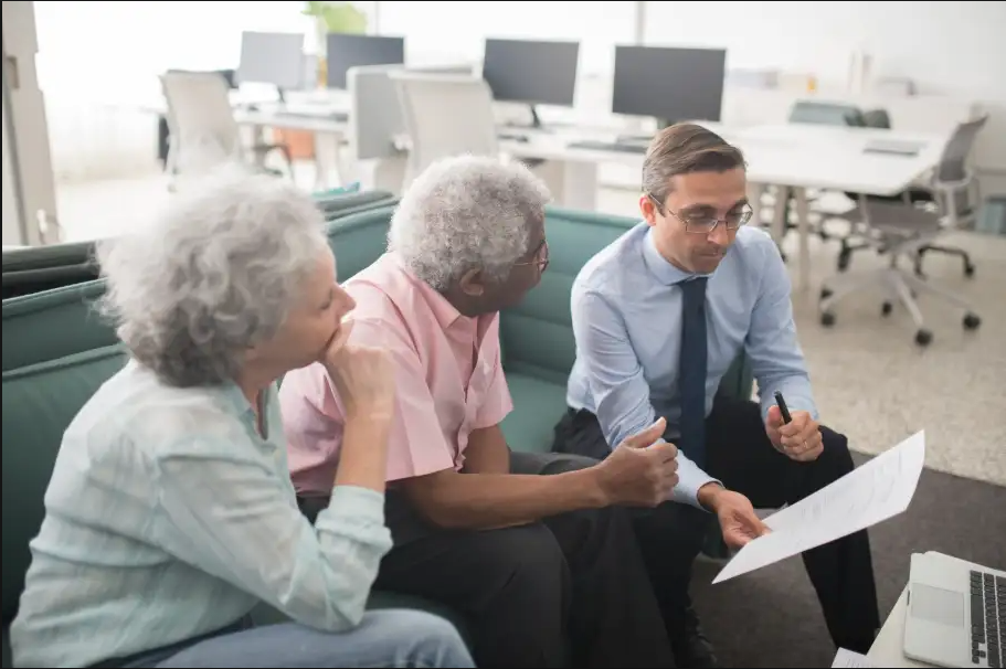 Three coworkers review a document together in a bright office with computer monitors behind them.