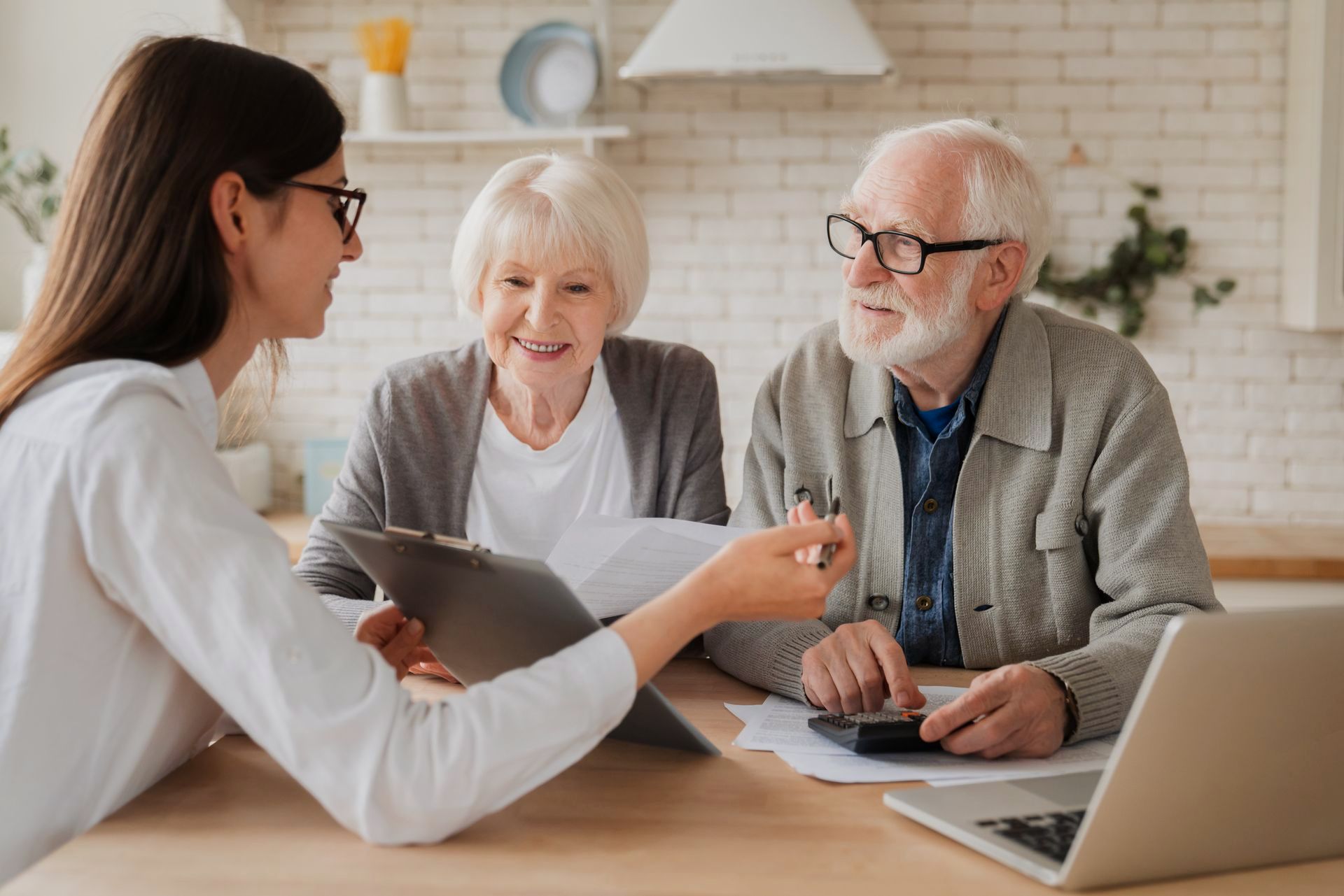 Financial advisor reviewing documents with elderly couple at a table, using a calculator and laptop.