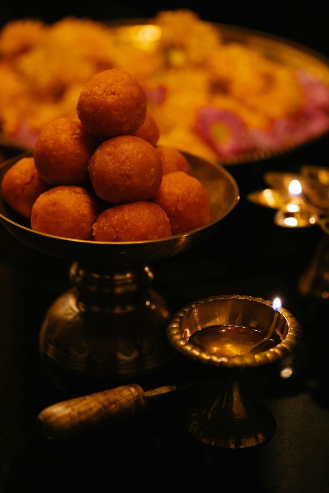 A bowl of round fried sweets with lit oil lamps in a warm, dim festive setting