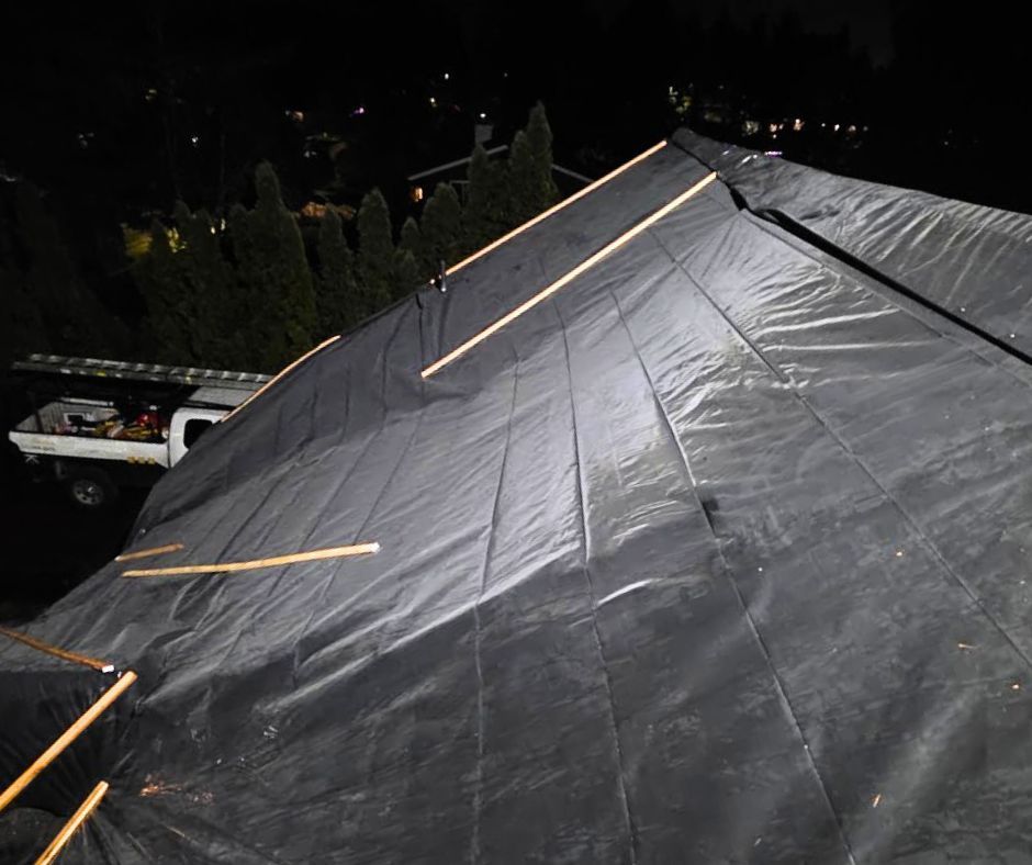 Rain-soaked black tarp over a sloped roof at night, with a vehicle and trees in the background