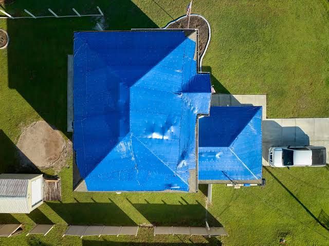 Aerial view of a house with a bright blue roof, driveway, and green lawn.