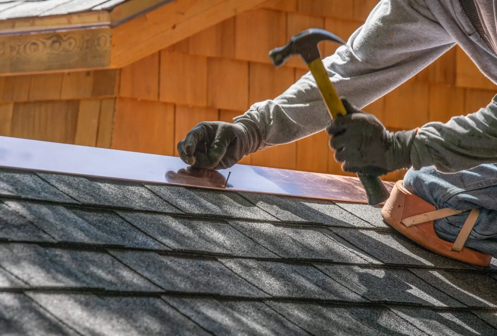 Roofers installing shingles with a hammer on a gray roof against a wooden house wall