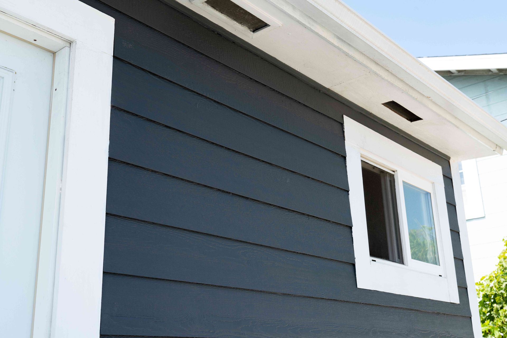 Close-up of a house exterior with dark blue siding and a white-framed window under the eaves
