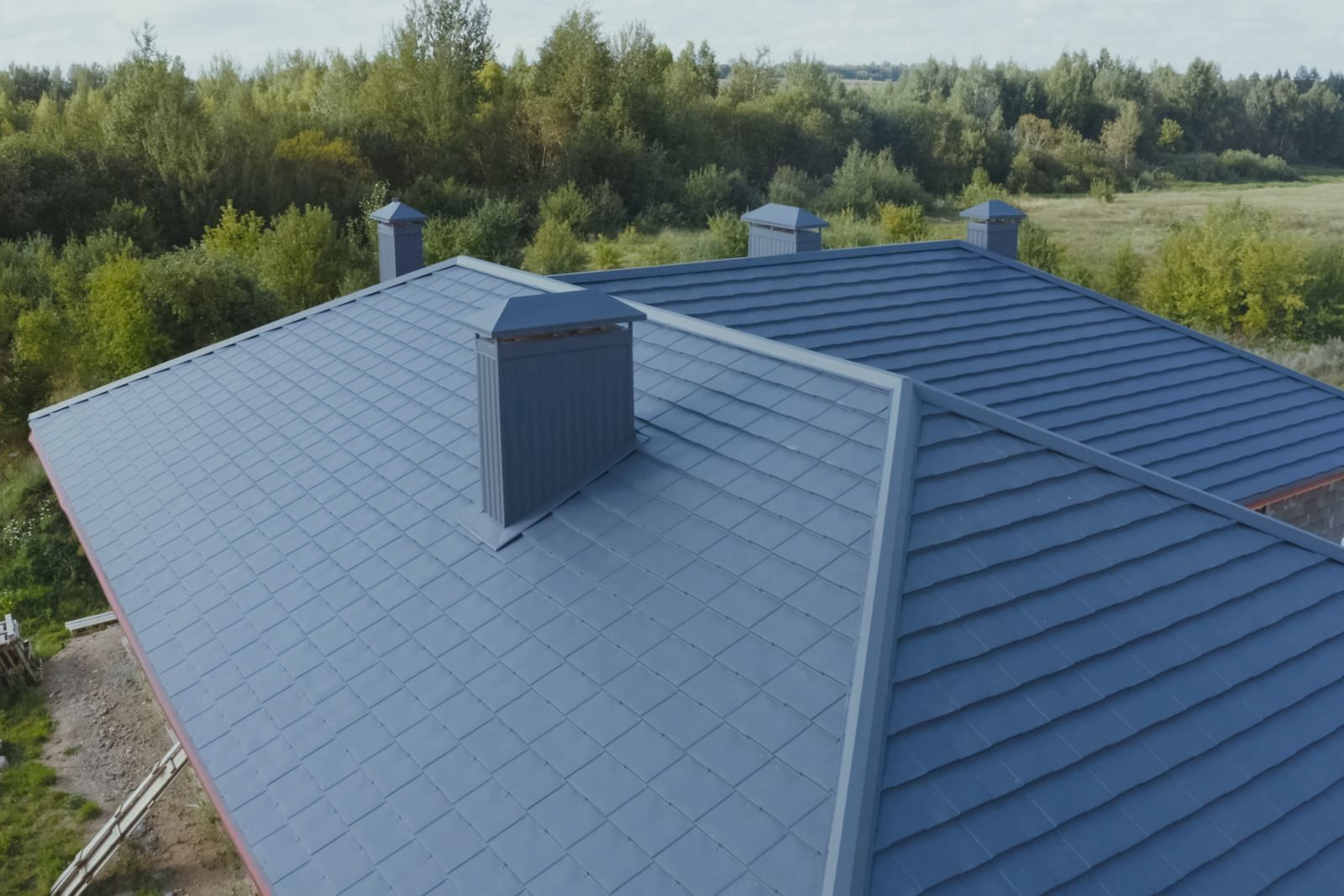 Blue metal roof with skylight and chimney, surrounded by trees and greenery