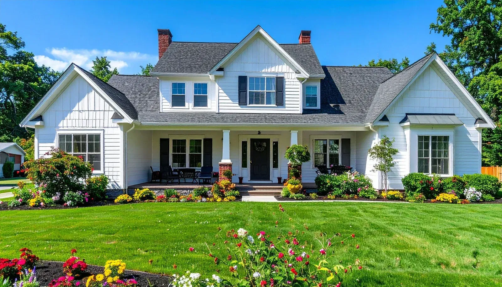 White suburban house with a front porch, flower garden, and neatly trimmed green lawn under a blue sky