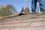 Worker standing on a shingled roof near a chimney during roof repair