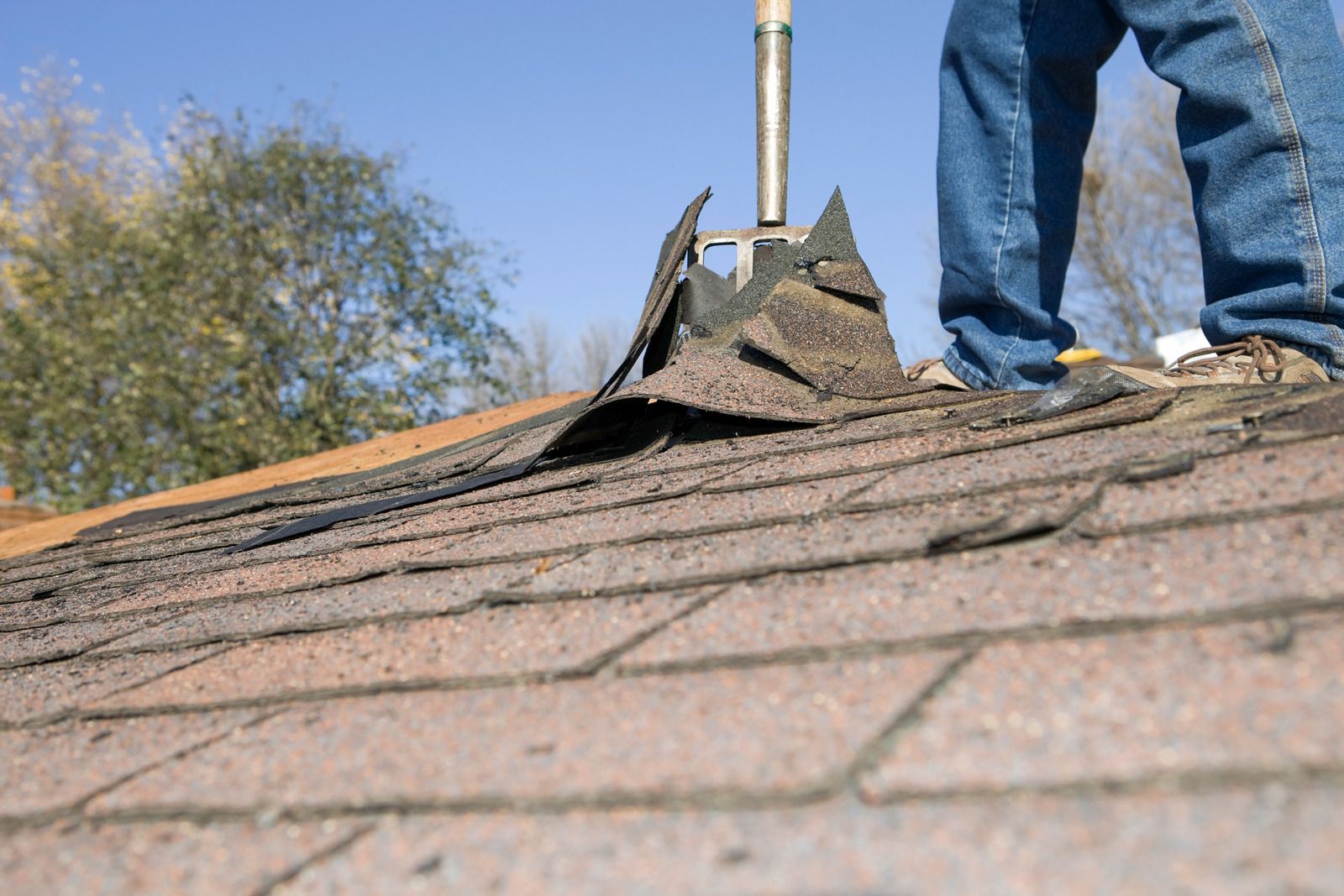 Worker standing on a shingled roof near a chimney during roof repair