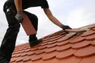 Worker installing red roof tiles on a sloped roof