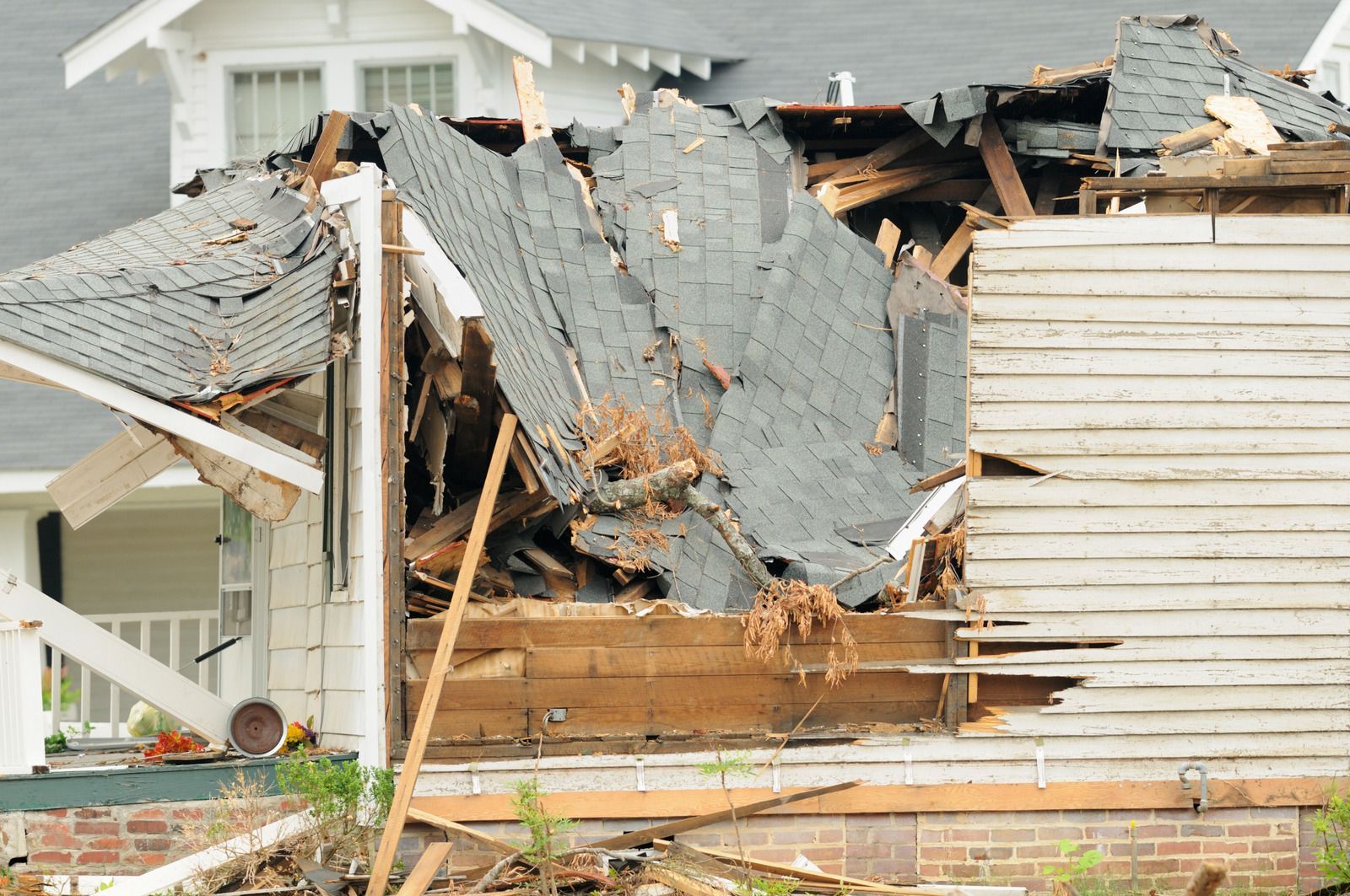 Severely damaged house with collapsed roof and broken siding, showing debris and exposed wooden framing.