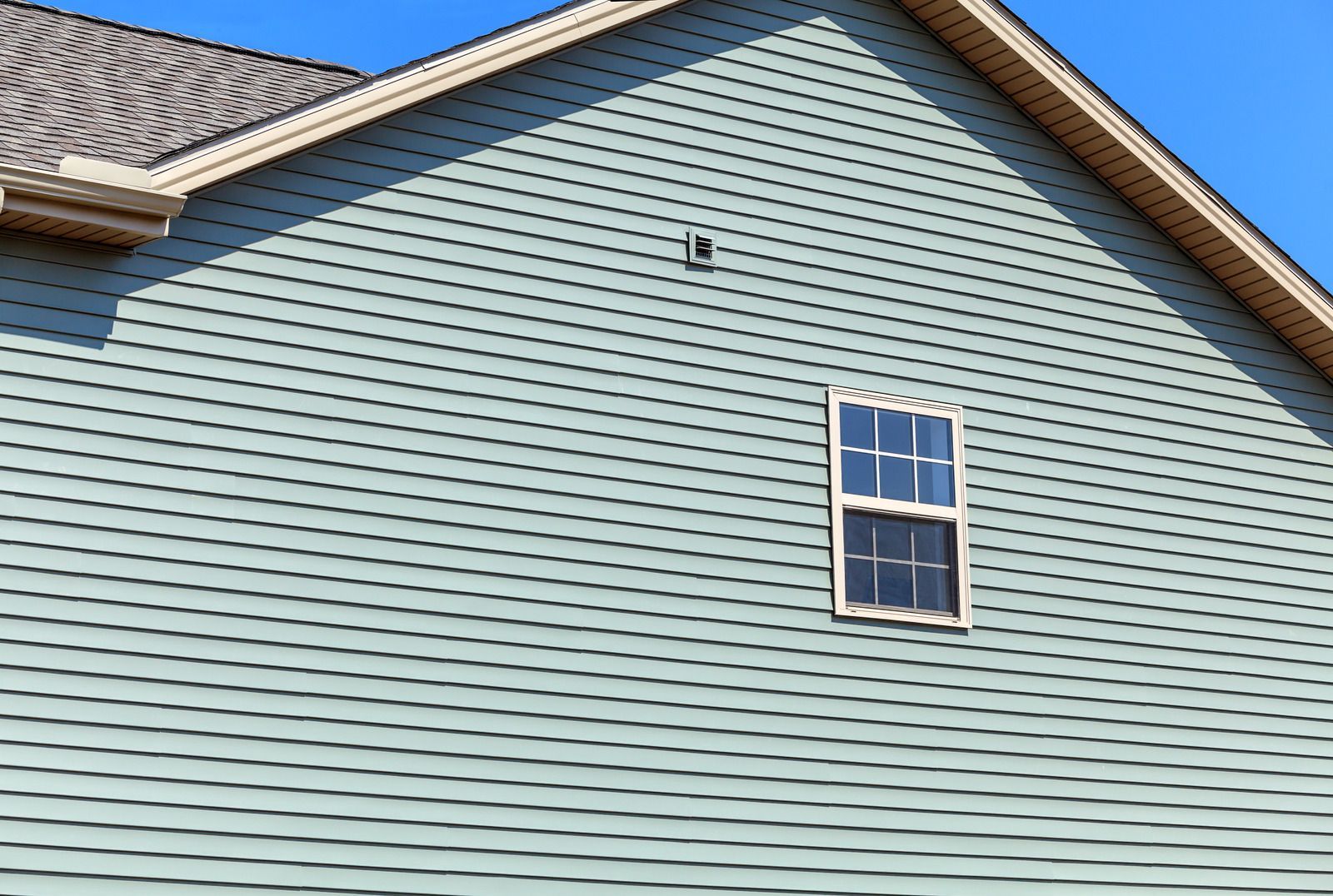 Light blue house siding with a small white-trimmed window and roof peak visible