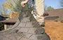 Worker removing damaged shingles from a roof during repairs