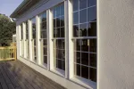 Exterior of a house with tall white-framed windows and a wooden deck in sunlight