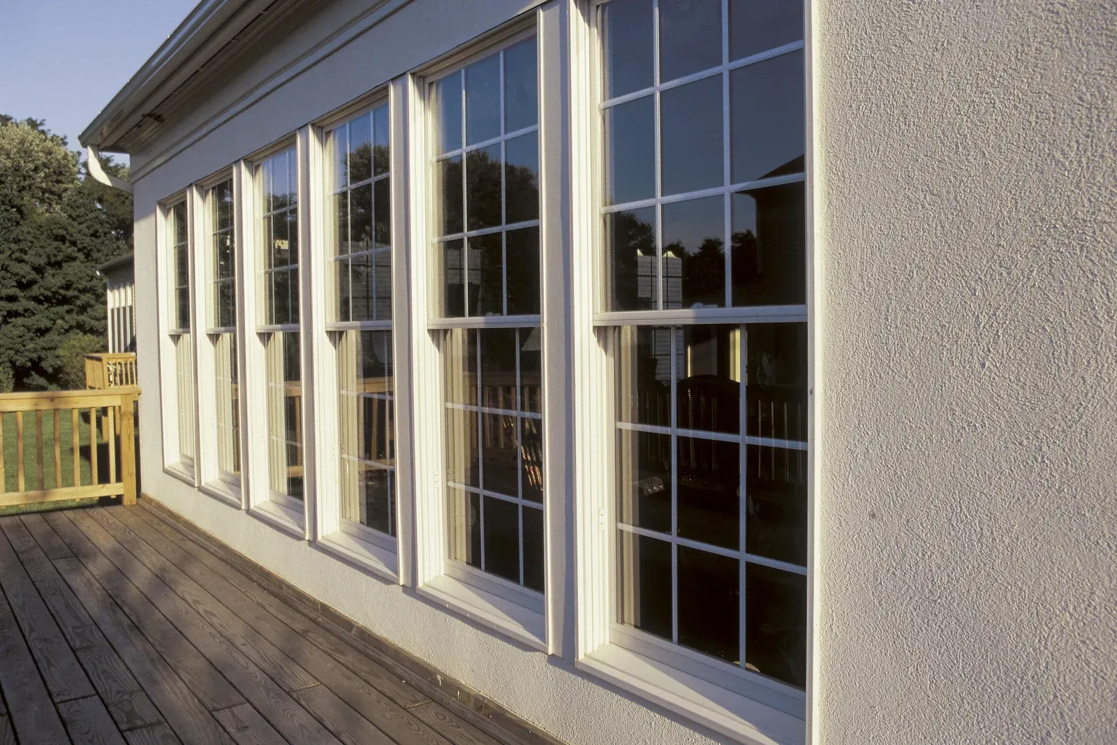Exterior of a house with tall white-framed windows and a wooden deck in sunlight