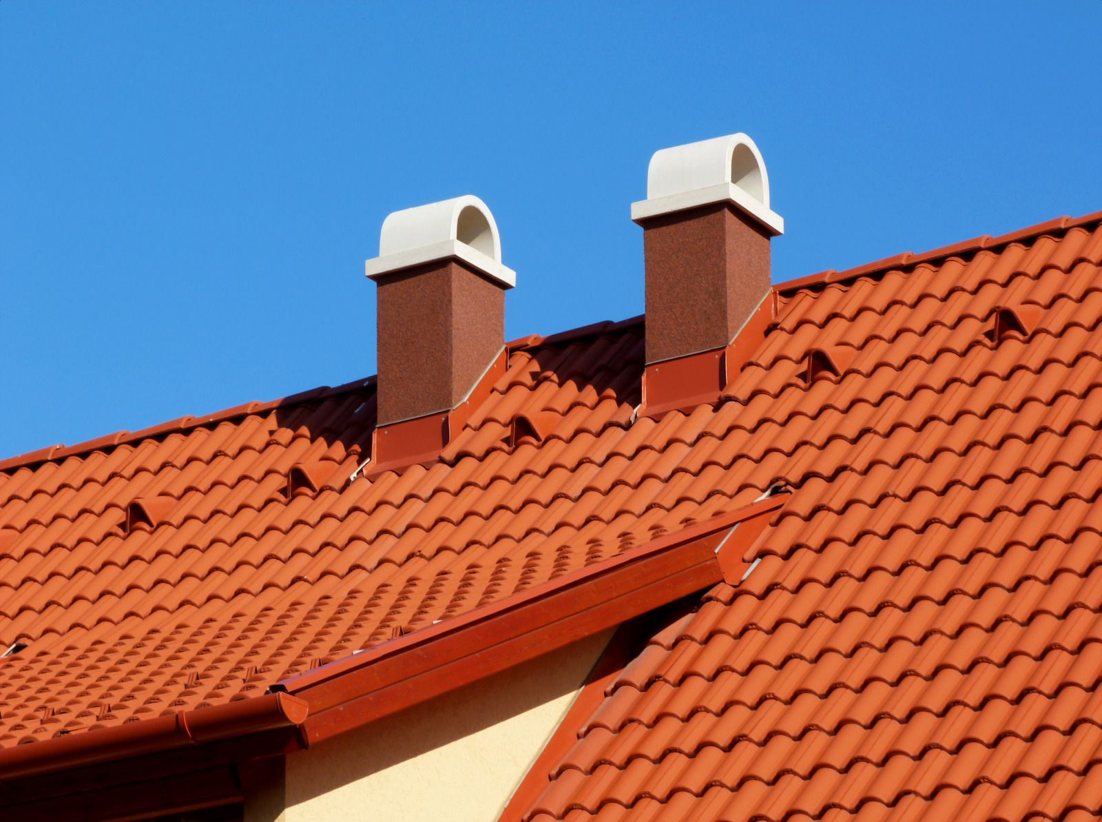 Red tiled roof with two brick chimneys against a blue sky