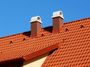 Red tiled roof with two brick chimneys against a blue sky