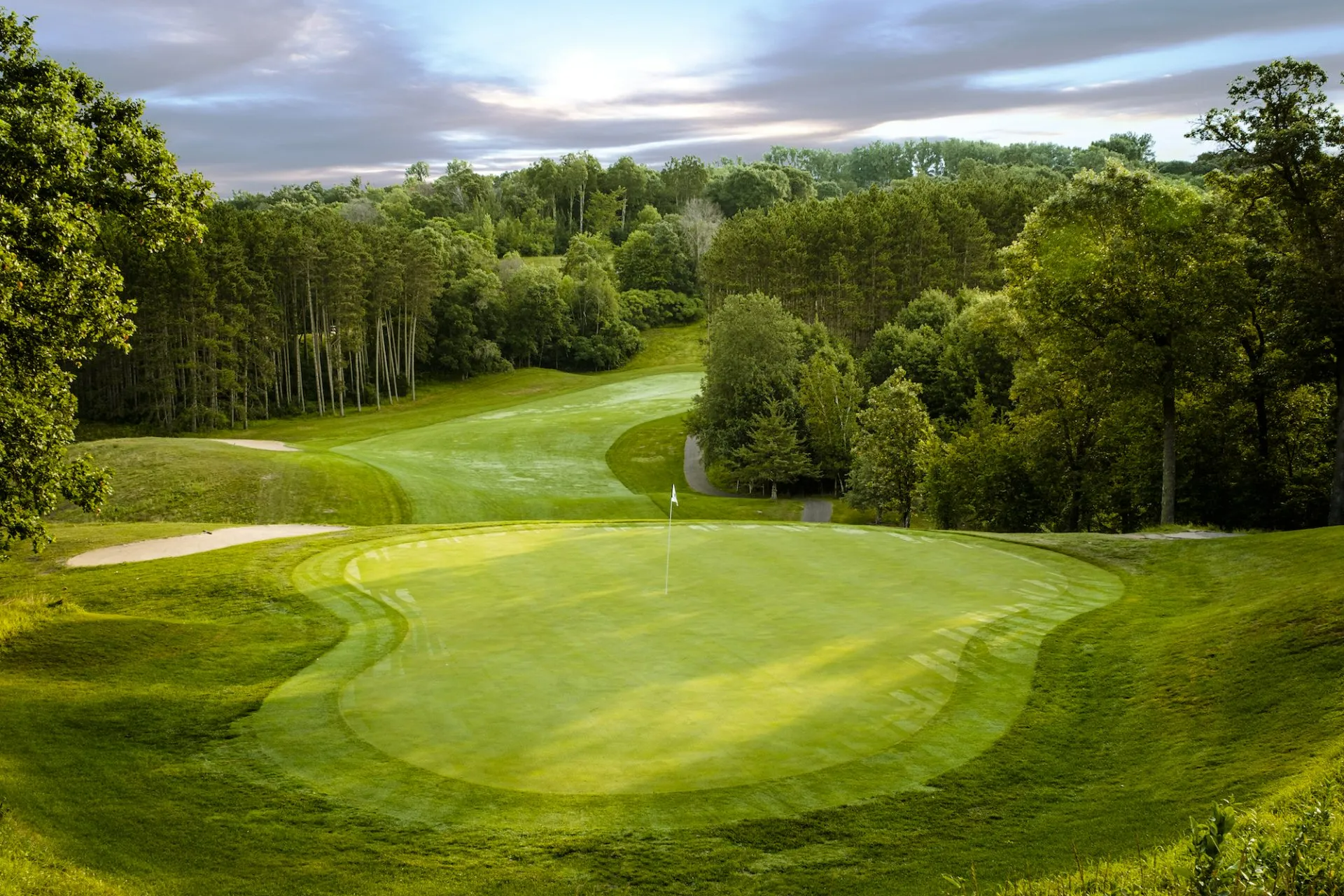 A golf course with a green and trees in the background.
