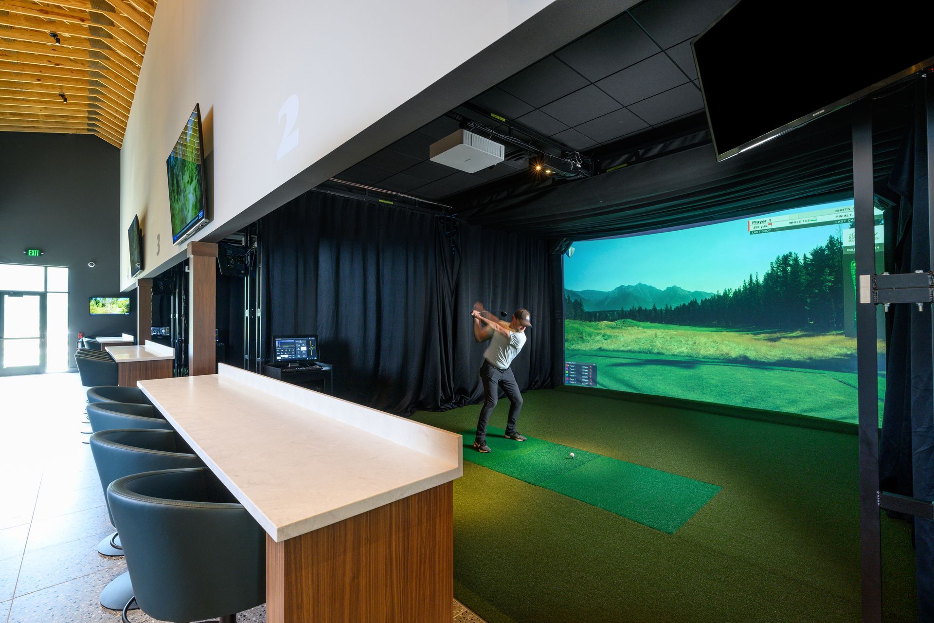A man is swinging a golf club in a golf simulator.