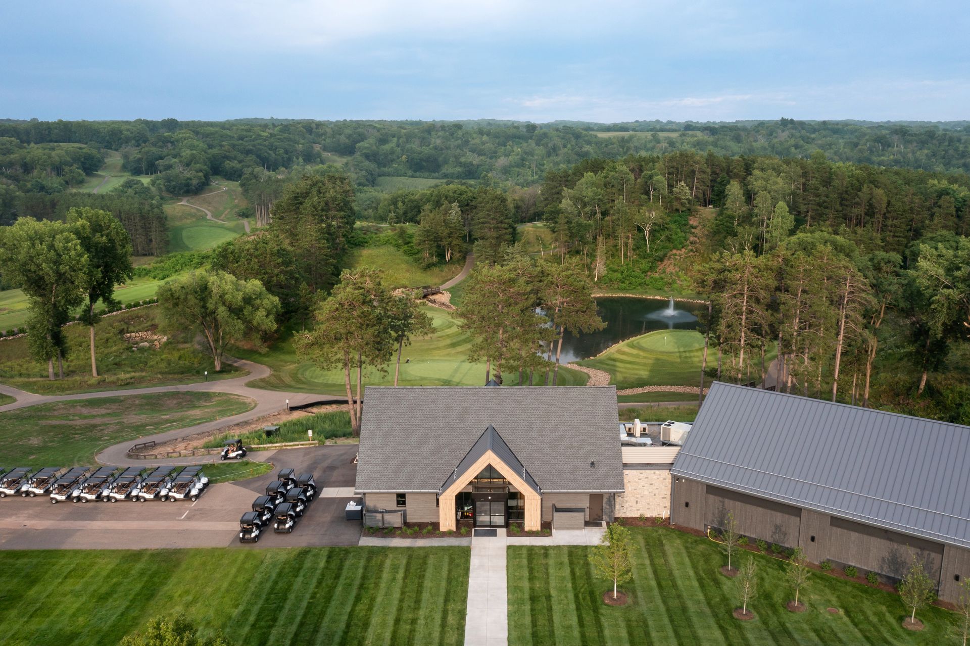 An aerial view of a large house in the middle of a lush green field surrounded by trees.