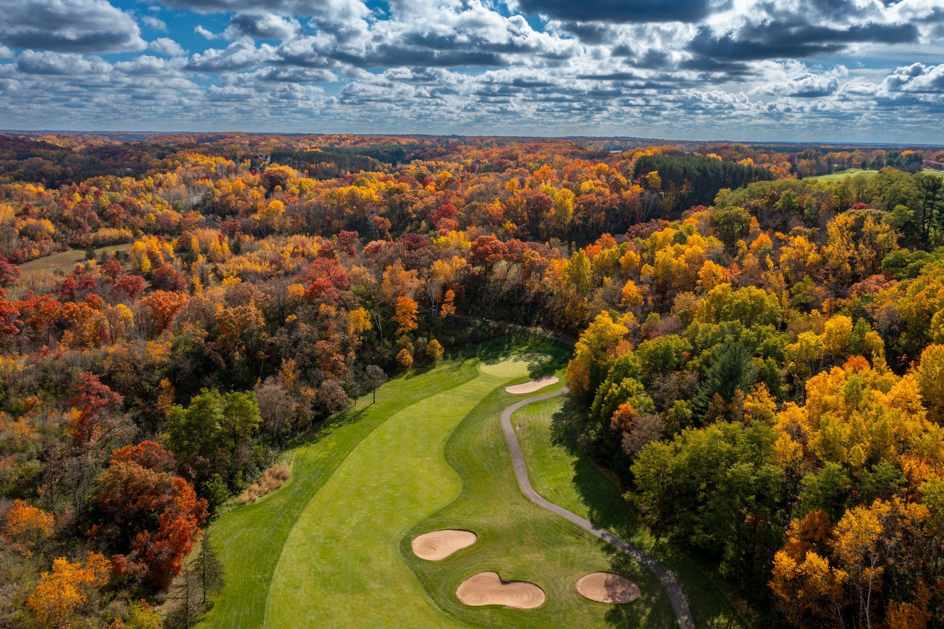 An aerial view of a golf course surrounded by trees in autumn.