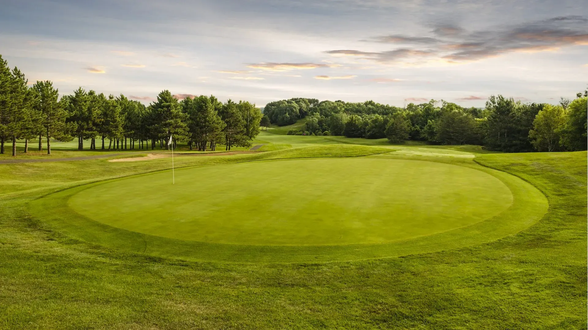 A golf course with a green and trees in the background.