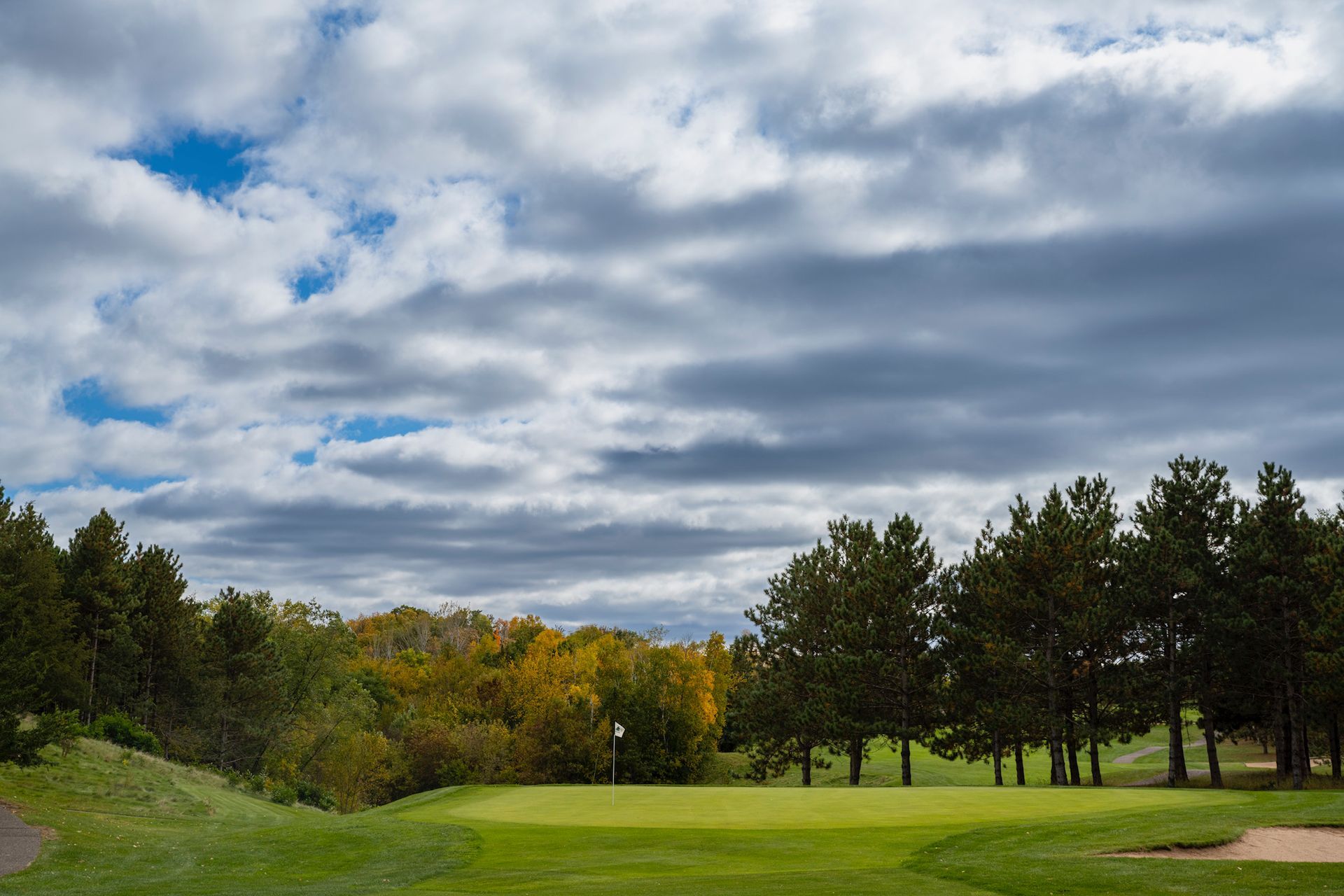 A golf course with trees and a cloudy sky in the background.