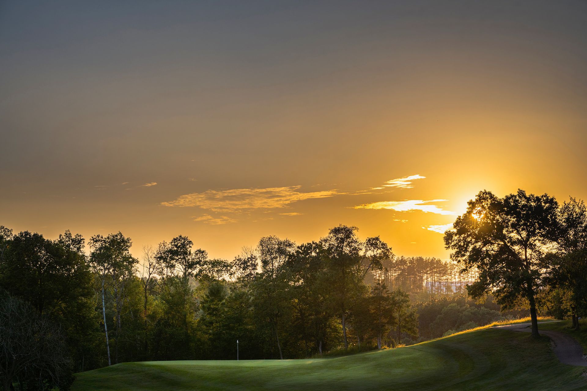The sun is setting over a golf course with trees in the foreground.