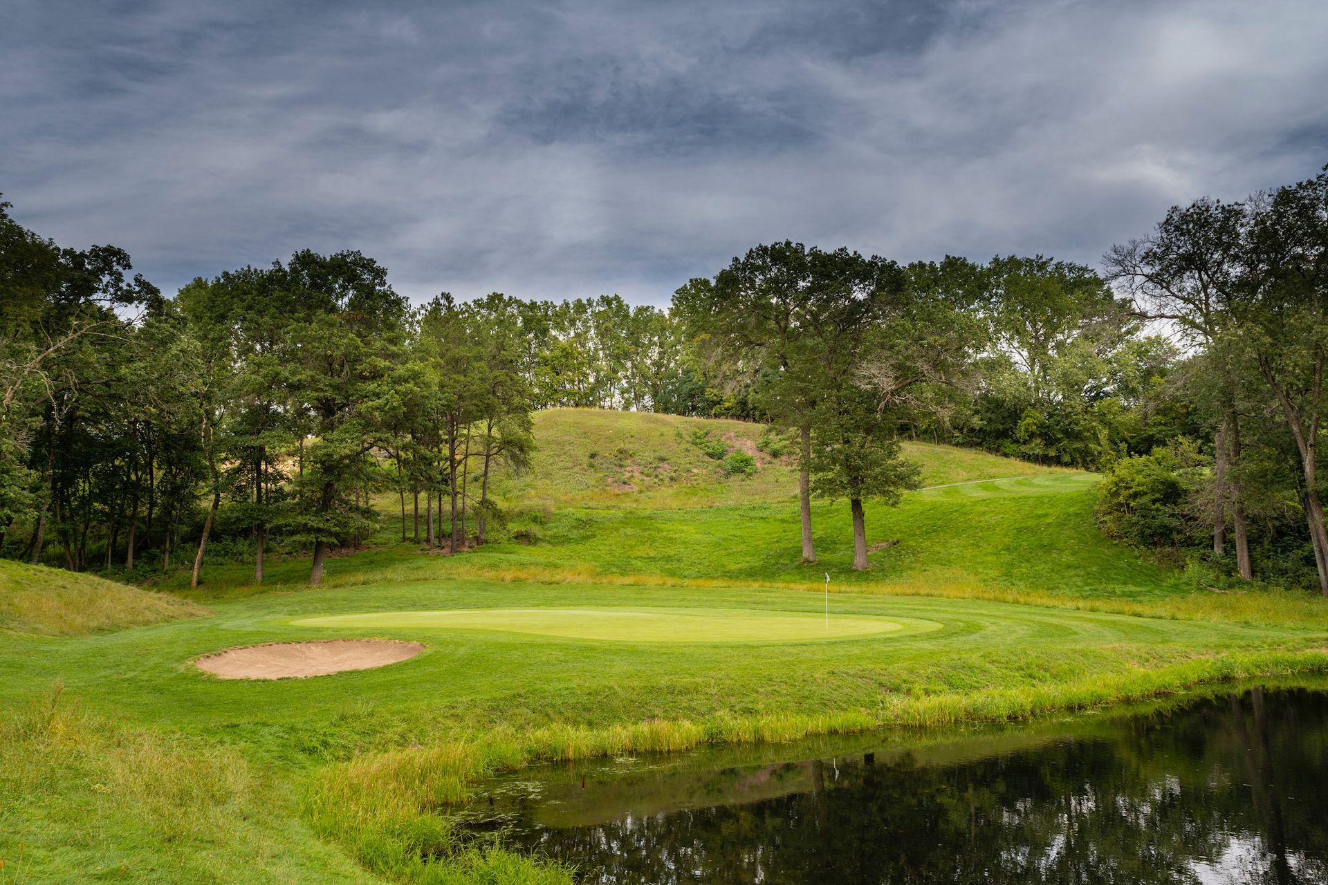 A golf course with a pond in the middle of it and trees in the background.