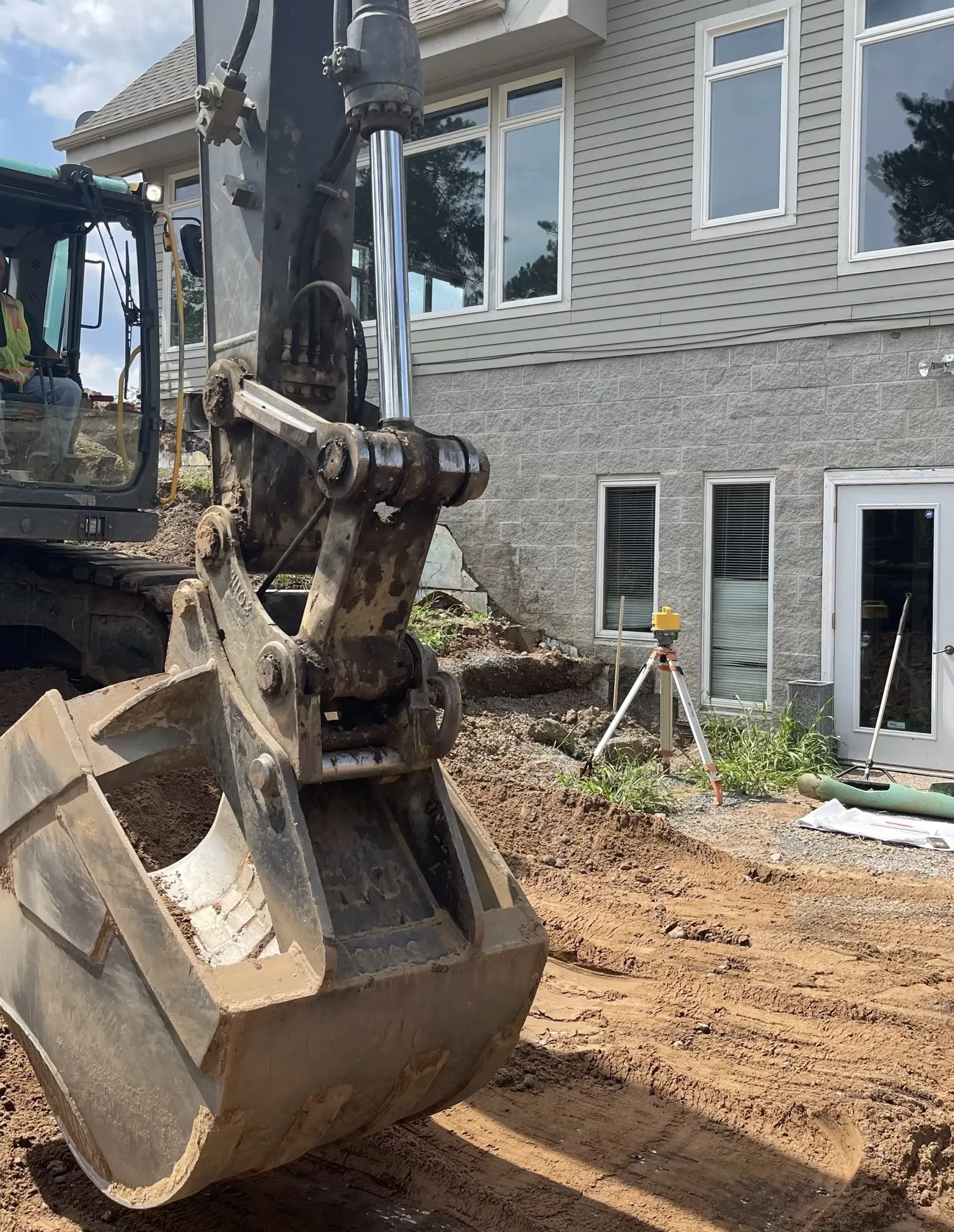 A large excavator is digging in the dirt in front of a house.