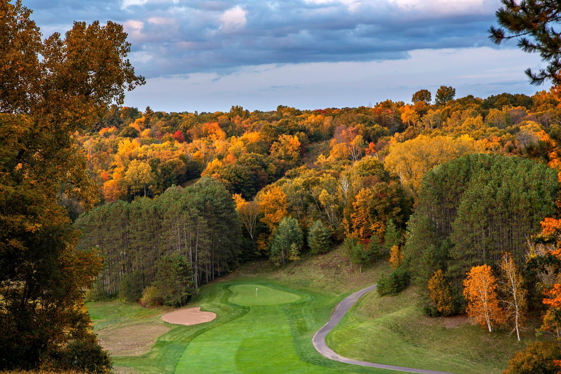 A view of a golf course surrounded by trees with autumn leaves.