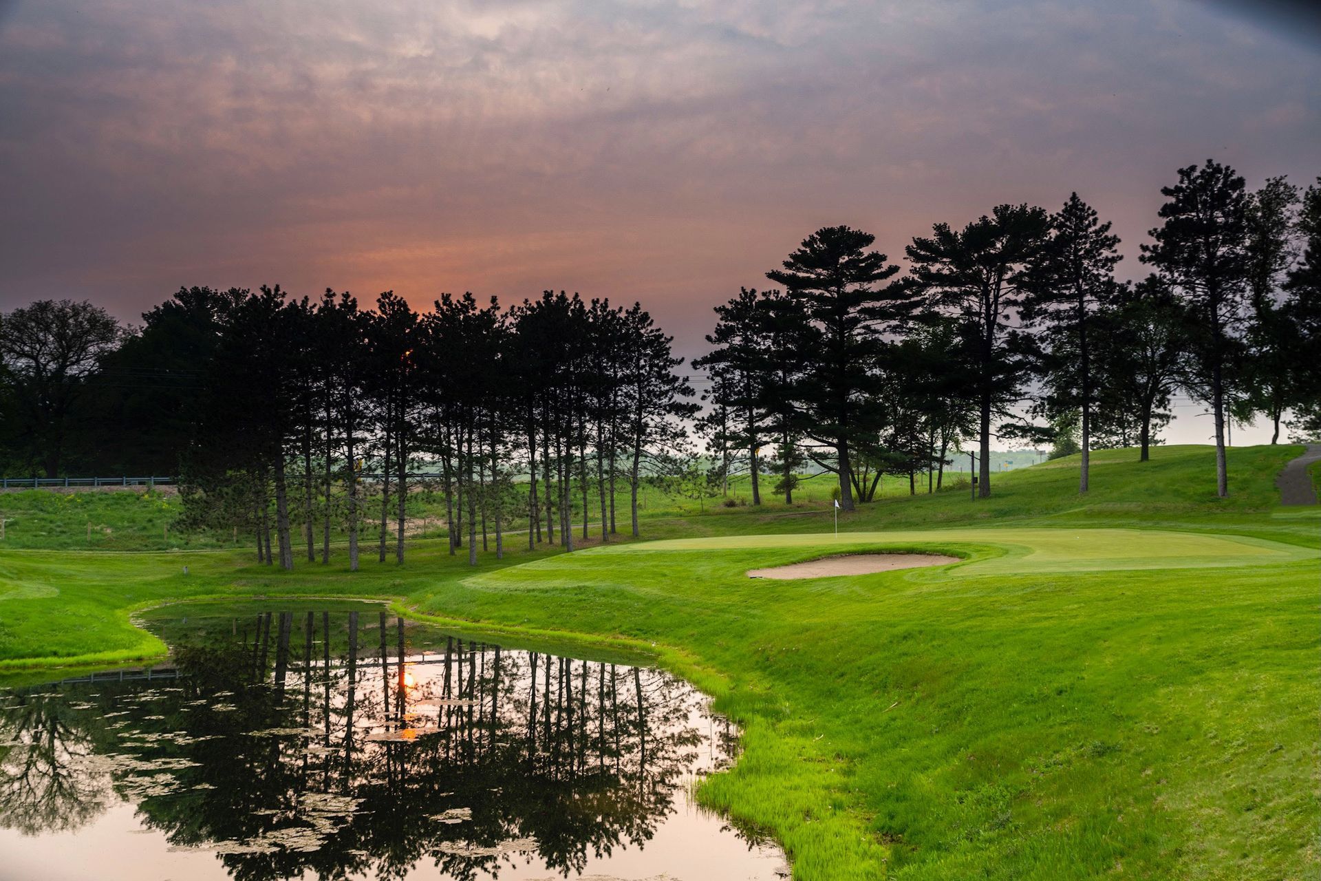 A puddle in the middle of a golf course with trees in the background