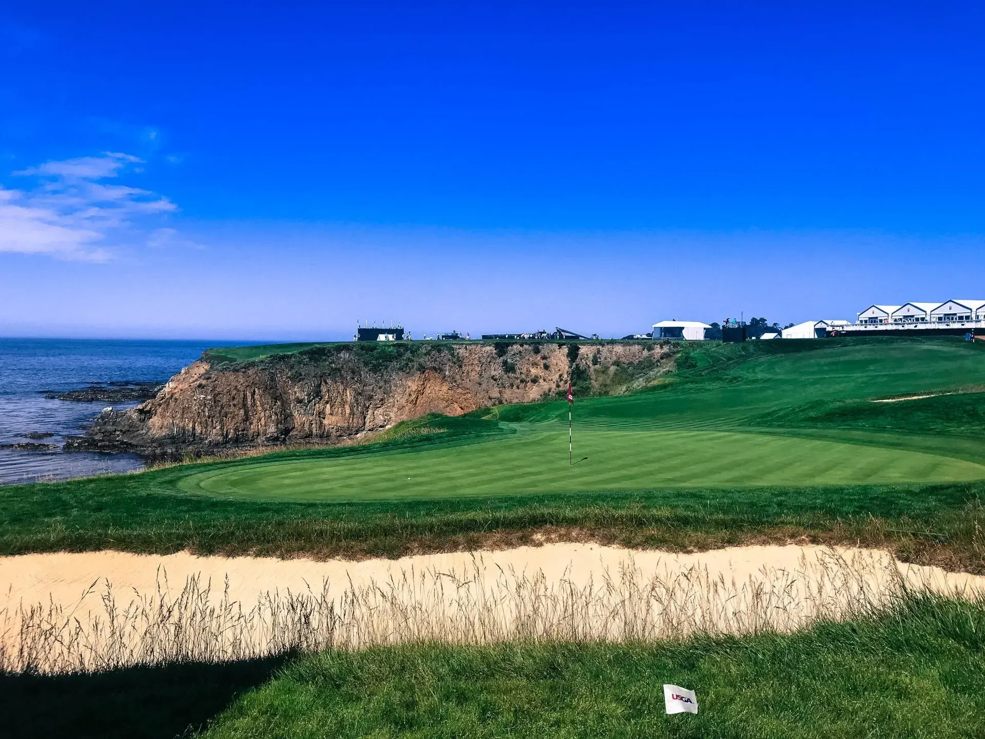 A golf course with a green and sand dunes on a cliff overlooking the ocean.