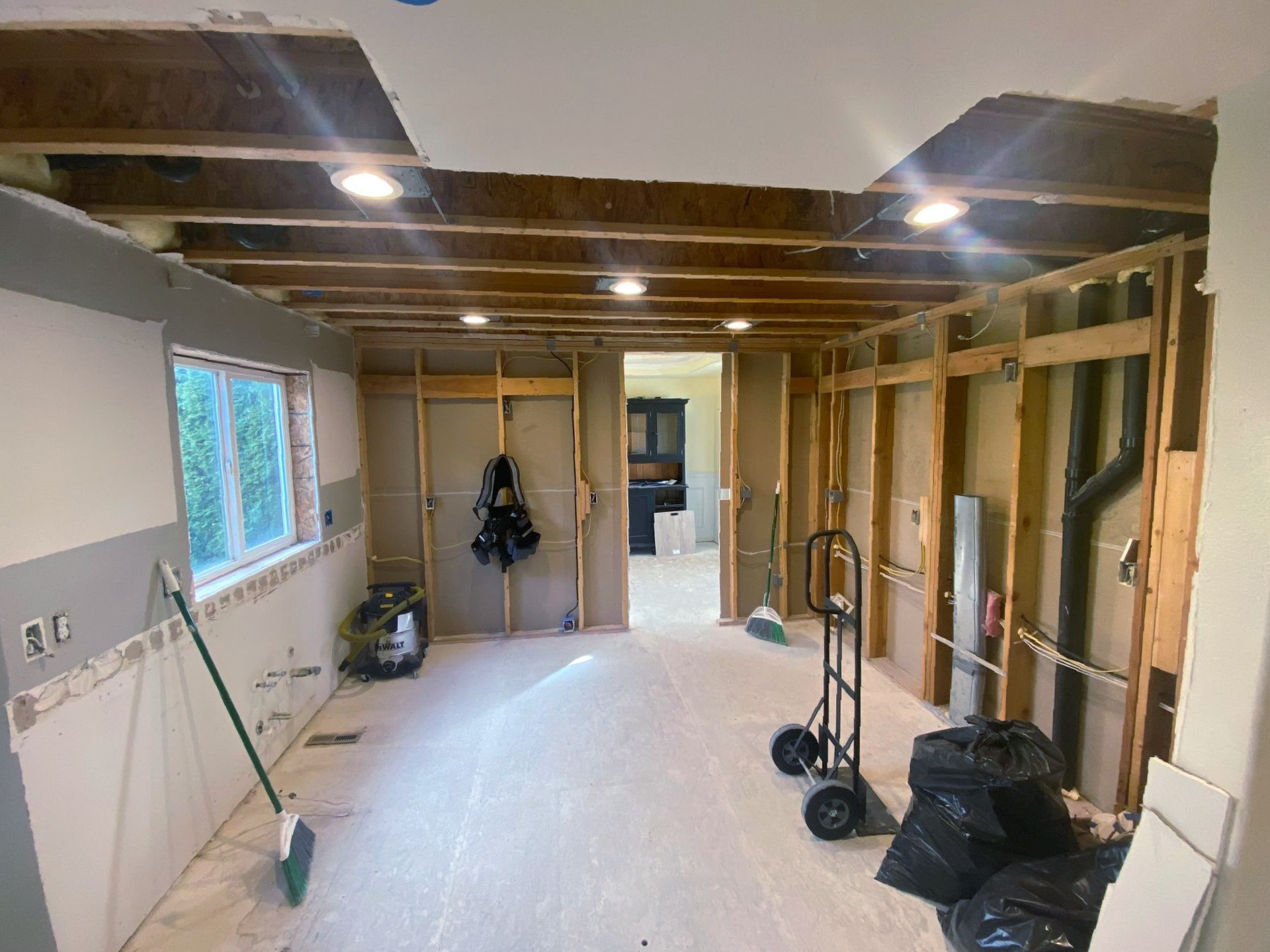 Partially gutted room under renovation with exposed studs, ceiling joists, tools, and debris on the floor