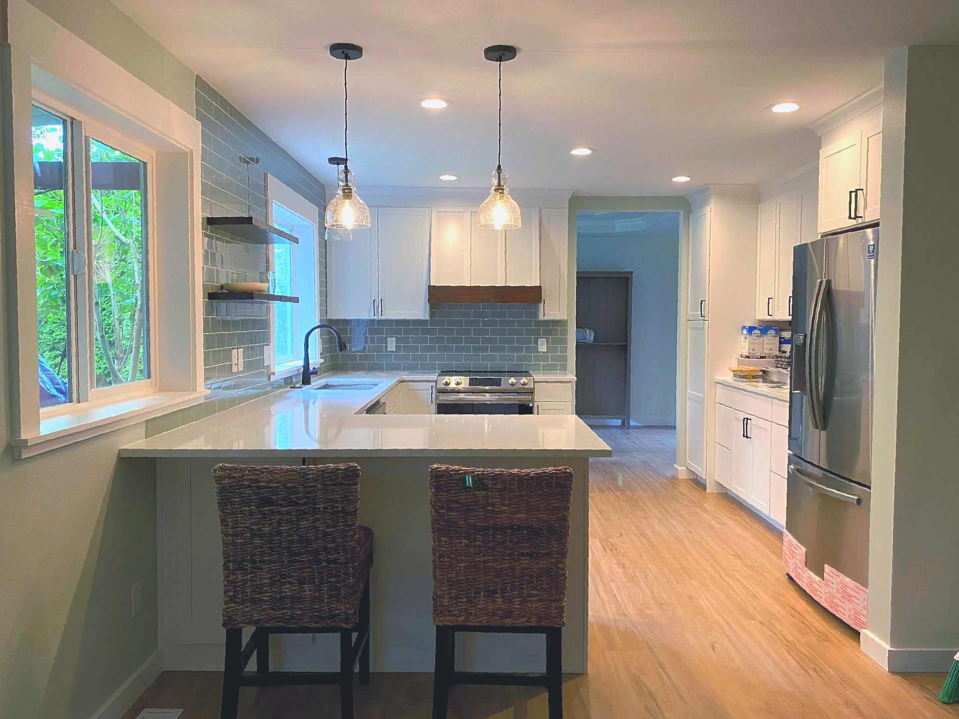 Modern kitchen with white cabinets, island seating, pendant lights, and a large window overlooking greenery