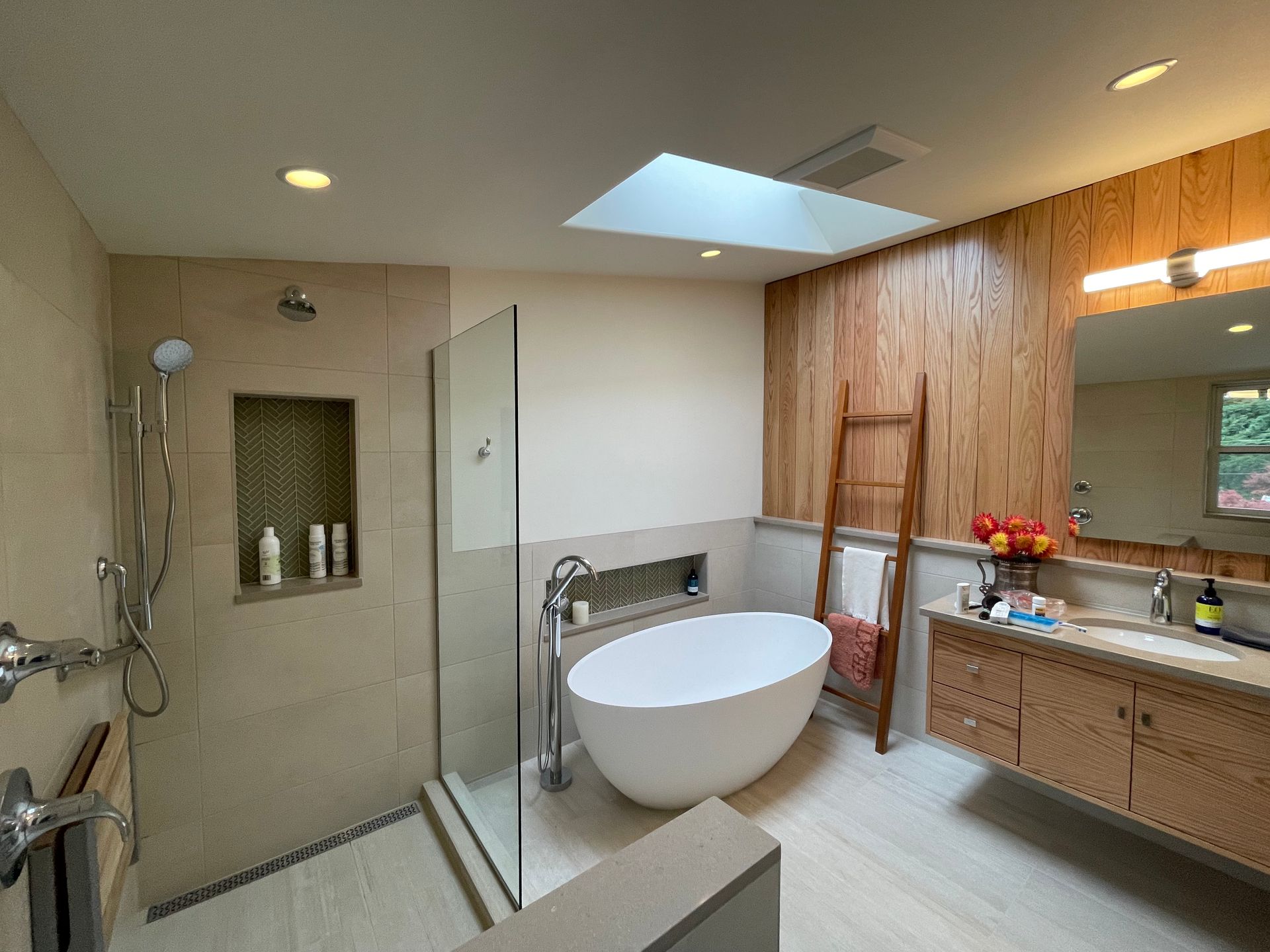 Modern bathroom with glass shower, freestanding tub, wood vanity, and skylight