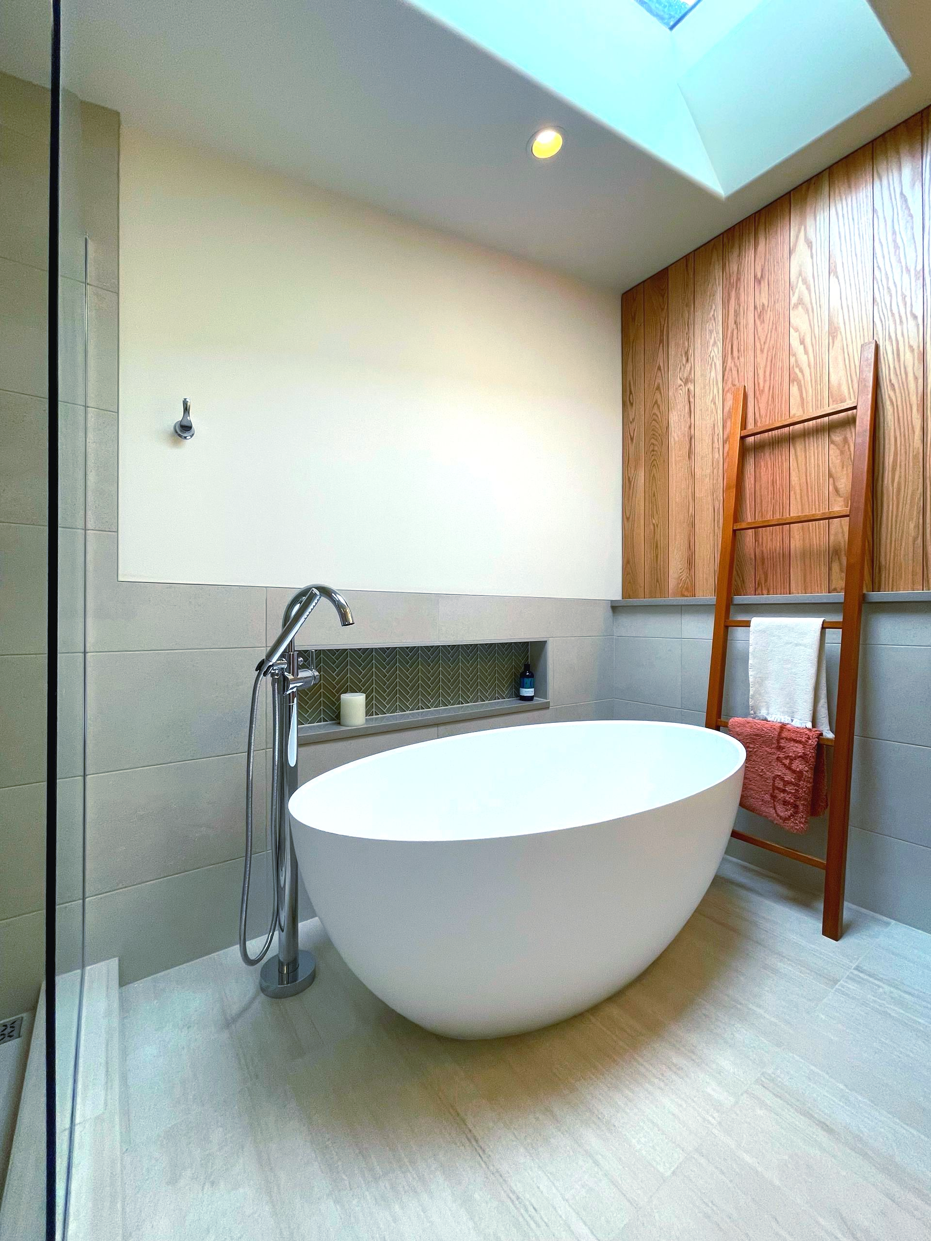 Modern bathroom with freestanding white tub, skylight, wood paneling, and towel rack