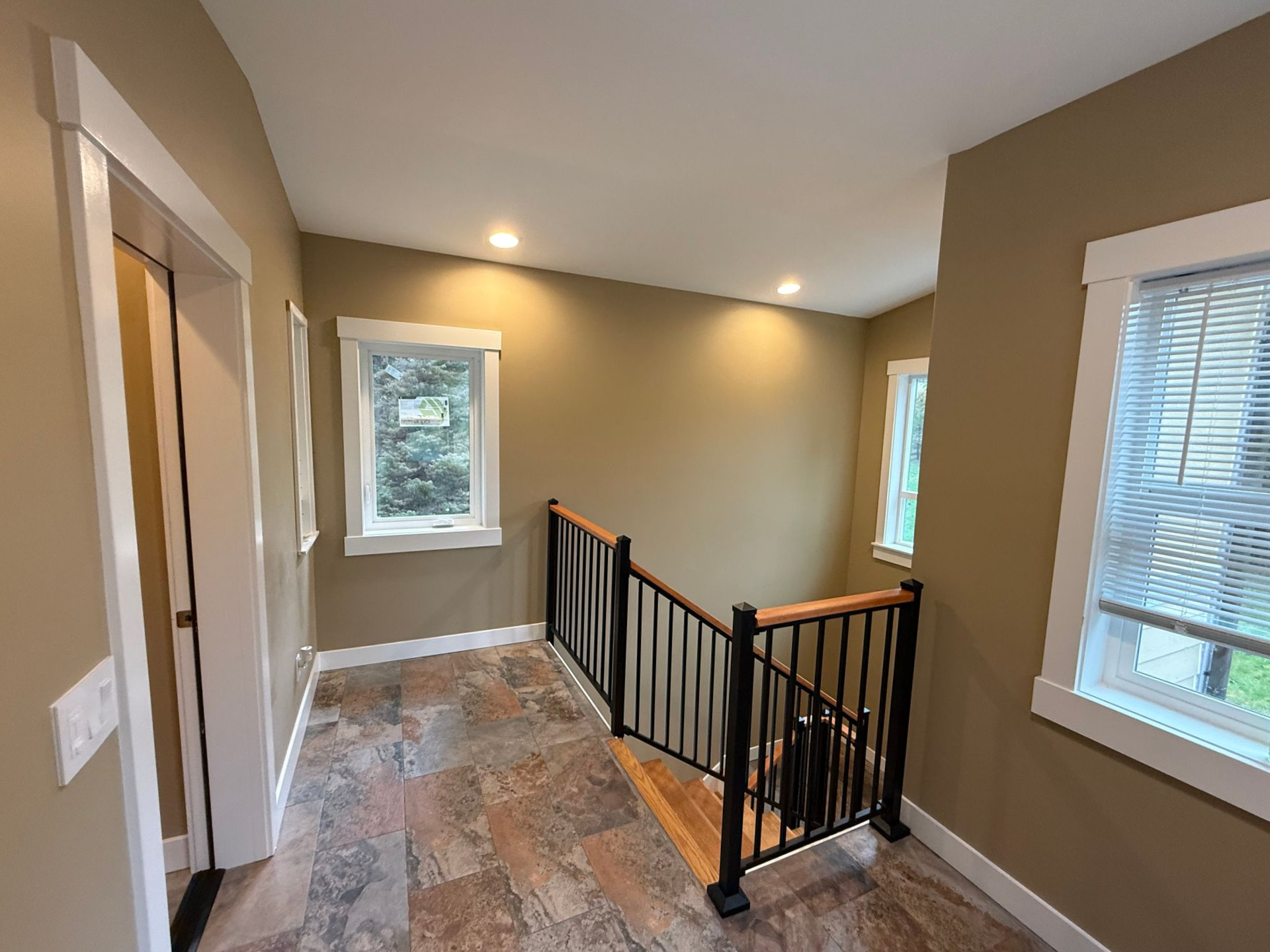 Upstairs hallway with beige walls, carpet, and a black railing overlooking stairs