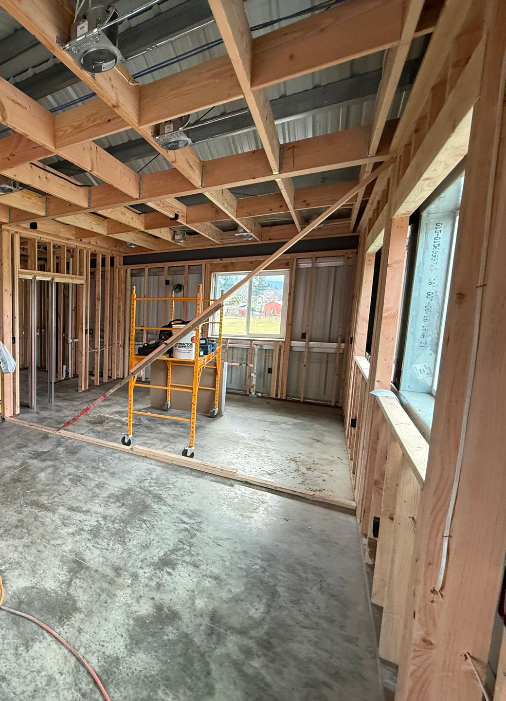 Unfinished room under construction with exposed studs, a ladder, and a large window.