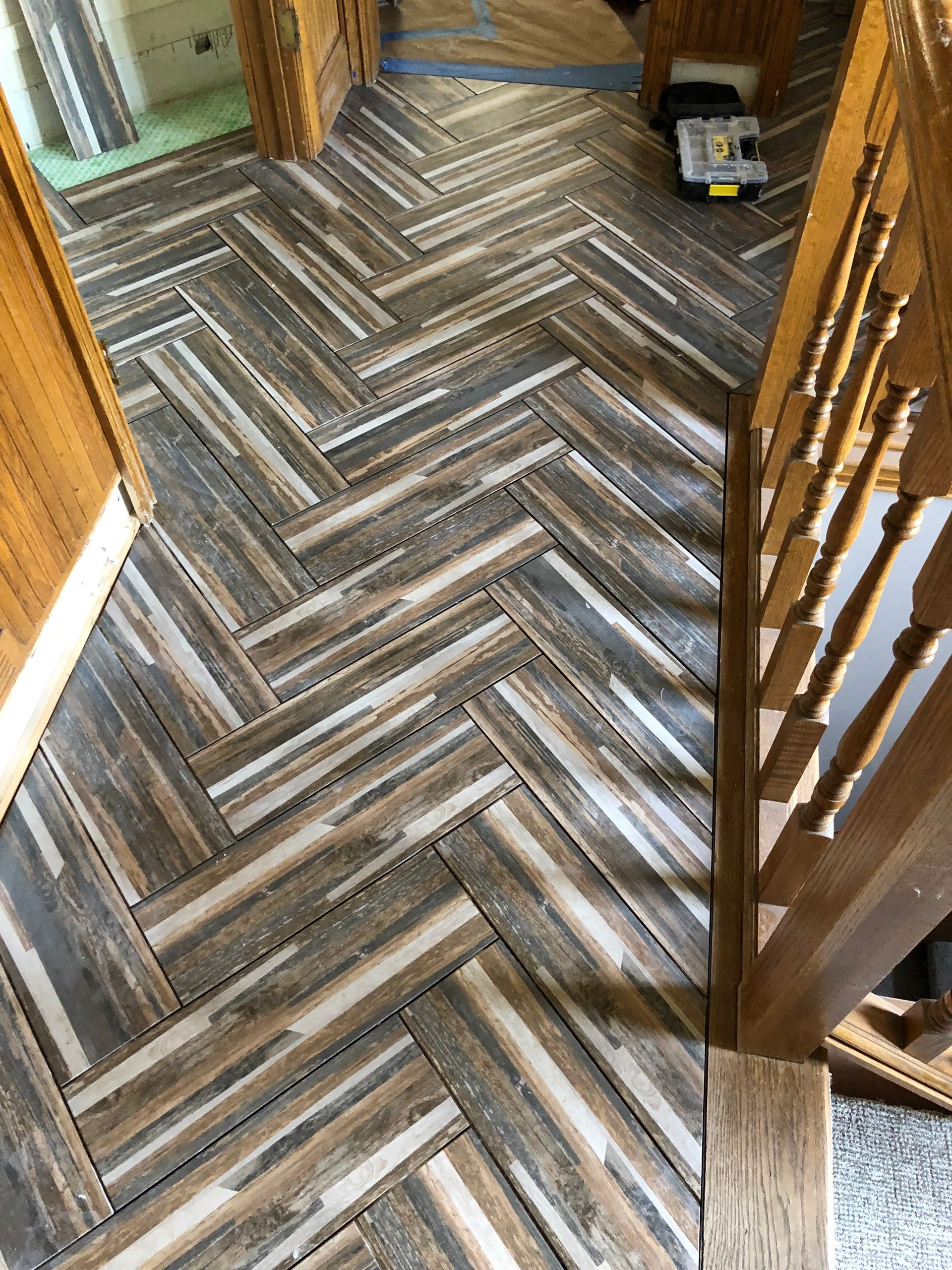 A herringbone tile floor in a hallway next to a staircase.
