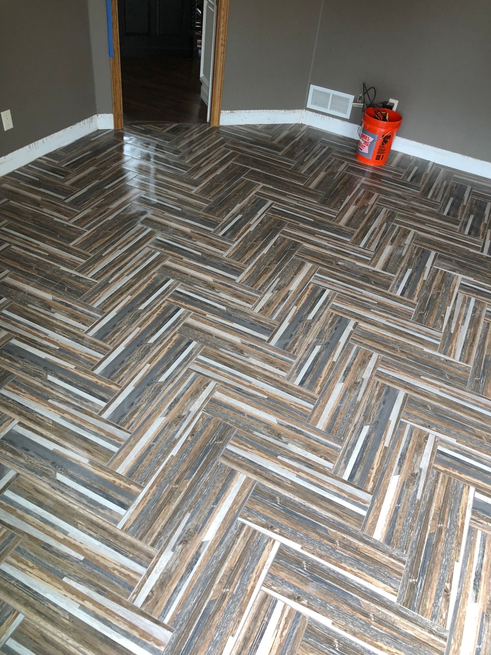 A room with a herringbone tile floor and a bucket on the floor.