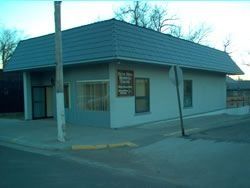 Blue-gray building with a slanted roof on a corner lot, a sign by the door, and a street sign.