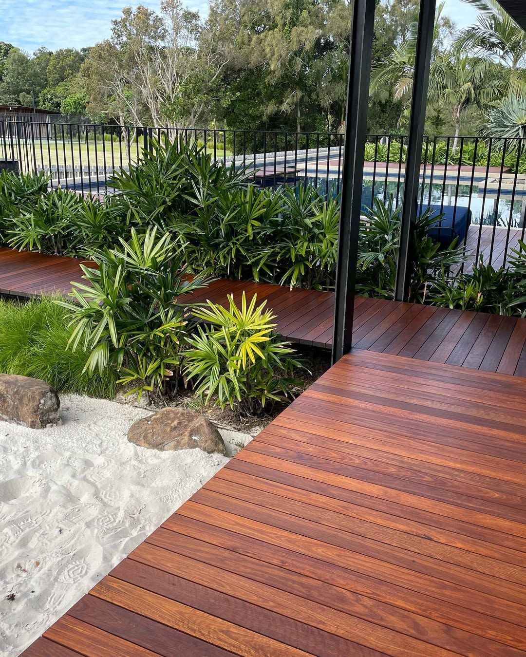 Wooden Deck Path With Sand Garden and Lush Green Plants Leading to a Pool Area — CM Timber Flooring in Byron Bay, NSW