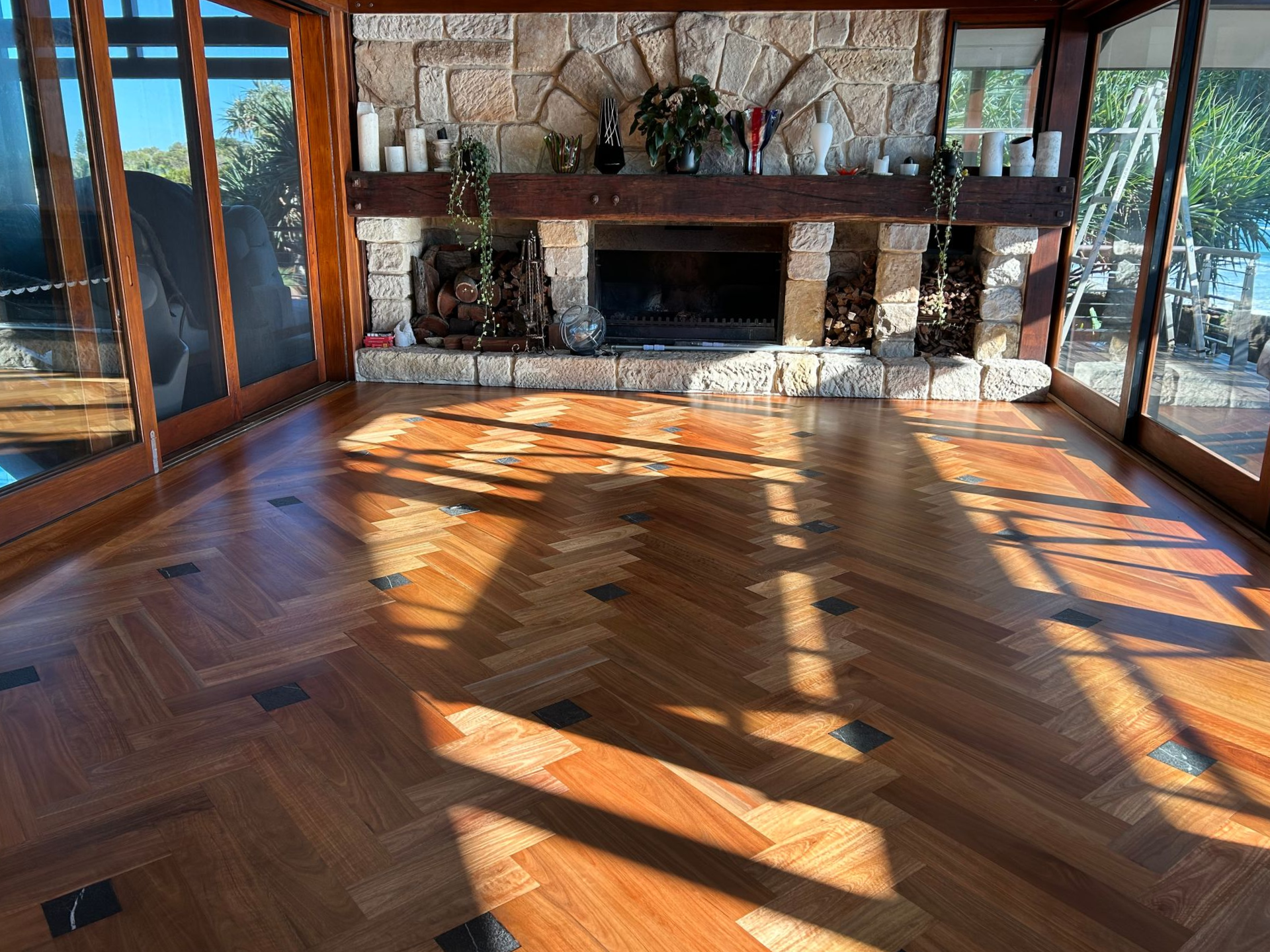 Wooden-floored room with stone fireplace, flanked by windows — CM Timber Flooring in East Ballina, NSW
