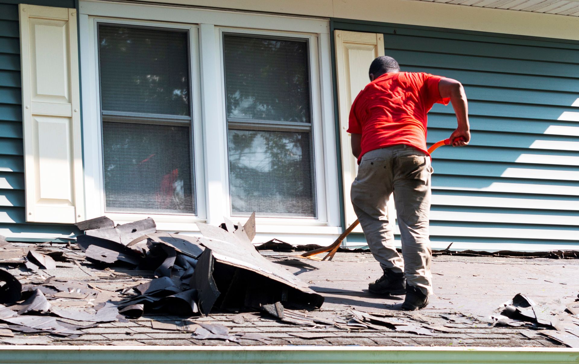 A man in a red shirt is working on the roof of a house.