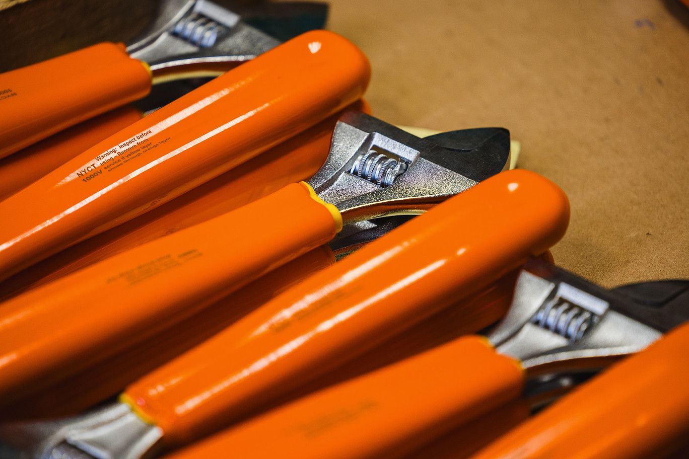 A pile of adjustable wrenches with bright orange insulated handles, angled closely together.