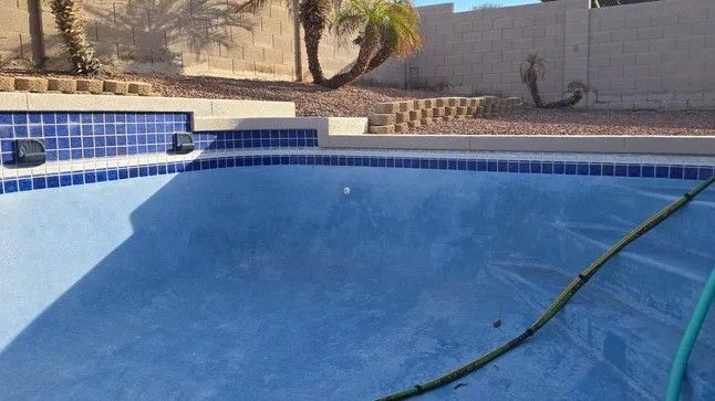 Empty blue swimming pool with a hose draped across it and desert landscaping in the background
