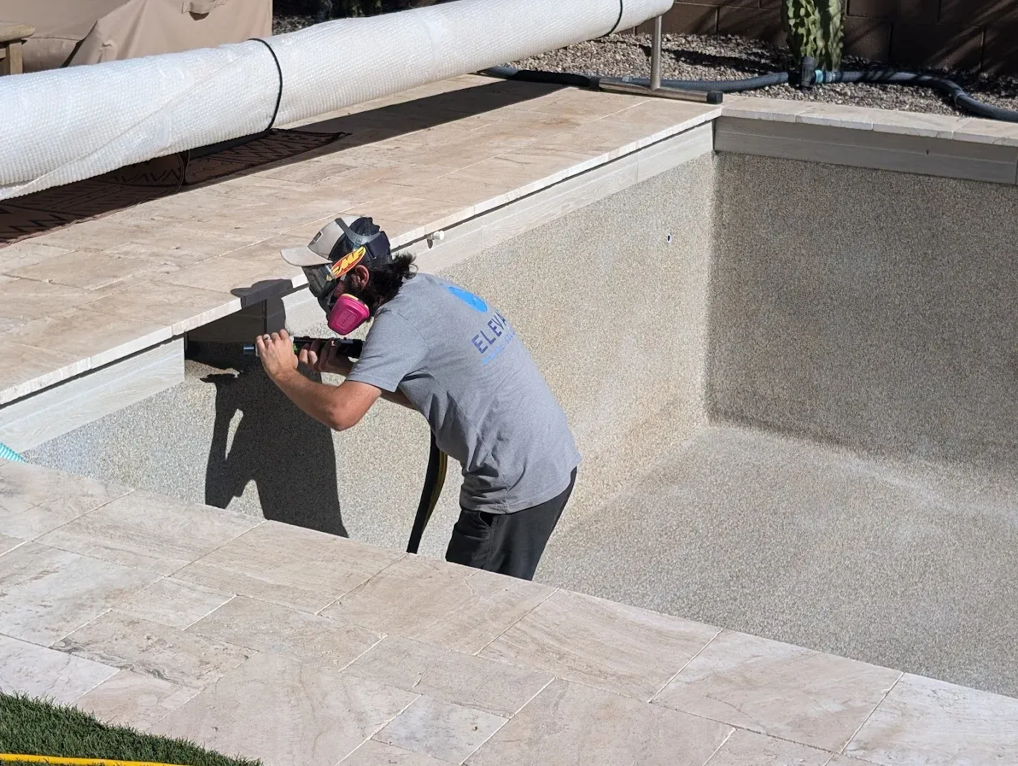 Matt a pool technician in safety gear cleaning the calcium line off residential pool tile