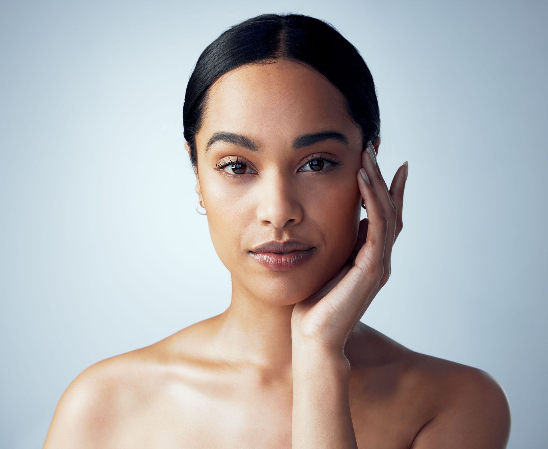 A woman is touching her face with her hand and looking at the camera.