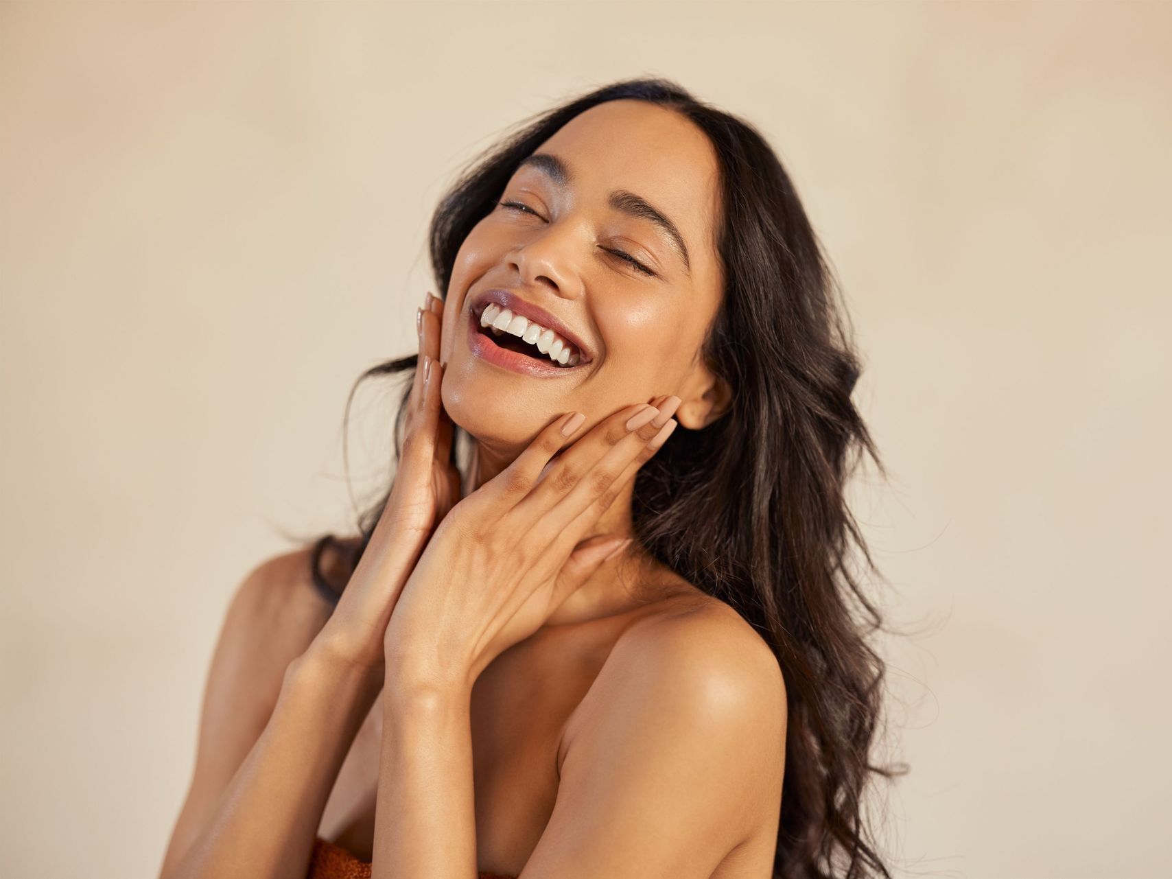 A woman is smiling and touching her face with her hands.