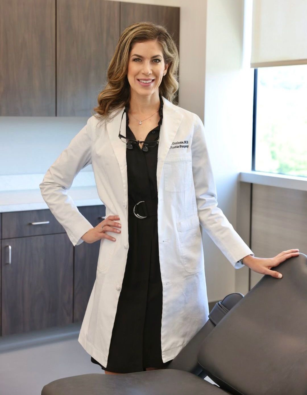 Dr. Ashley Guthrie wearing a white doctor's coat stands next to a patient exam chair